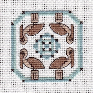 May include: A cross-stitch pattern featuring four brown pelicans with blue and white accents. The pelicans are arranged in a square pattern with their beaks pointing towards the centre.