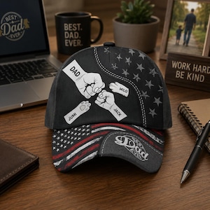 May include: A black baseball cap with a patriotic design. The cap features a graphic of two fists bumping, paw prints, and the text "DAD." The brim displays an American flag design and the text "Dad Ever."