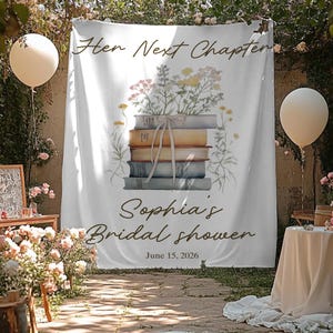 May include: A white backdrop with the text "Her Next Chapter" and "Sophia's Bridal shower" with the date June 15, 2026. The backdrop features a stack of books with flowers and a ribbon. Two cream-colored balloons are on either side.