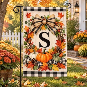 May include: A rectangular garden flag featuring a white wood-plank background with a black and white buffalo check border. The design includes a central letter S, a wreath of autumn leaves, pumpkins, pinecones, and a large striped fabric bow.