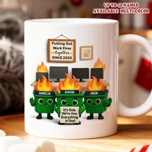 May include: White ceramic mug featuring a humorous design with green trash can characters labeled Amelia, David, and Jack, with flames above their heads. The mug includes the text "Putting Out Work Fires together SINCE 2020" and "It's fine. We're fine. Everything is fine!"