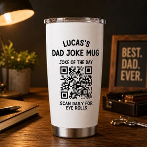 May include: A white stainless steel tumbler with a clear lid featuring black text that reads LUCAS'S DAD JOKE MUG, JOKE OF THE DAY, and SCAN DAILY FOR EYE ROLLS, along with a central black and white QR code printed on the front of the cylindrical vessel.