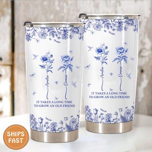 May include: Two white insulated tumblers with blue floral designs and the text "IT TAKES A LONG TIME TO GROW AN OLD FRIEND." Each tumbler has a name, "Amelia" and "Emma," in a script font. The design includes butterflies and dragonflies.
