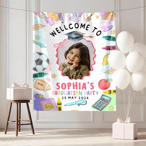 May include: A white graduation party banner with the text "WELLCOME TO" and "SOPHIA'S GRADUATION PARTY 29 MAY 2026". The banner features a photo of a girl, along with illustrations of school supplies, a soccer ball, and balloons.
