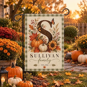 May include: A rectangular garden flag featuring a large letter S, a pumpkin, a sunflower, and a butterfly. The text reads Sullivan family and Est. 2026. The flag has a green and white checkered border and is displayed on a black metal stand.
