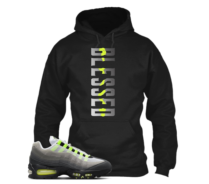 Op de afbeelding: Zwarte hoodie met het woord "BLESSED" in een verticaal ontwerp. De hoodie wordt gecombineerd met een grijze en zwarte sneaker met neon groene accenten.