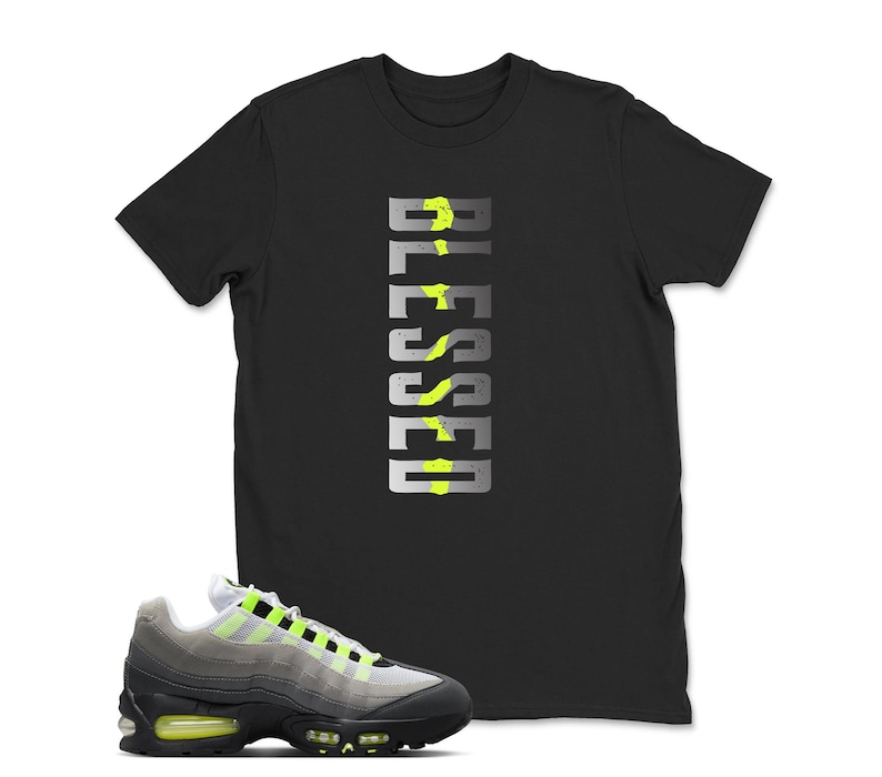 Op de afbeelding: Zwart T-shirt met het woord "BLESSED" in een verticaal ontwerp met neon groene accenten. Een paar grijze en zwarte sneakers met neon groene details staan op de voorgrond.