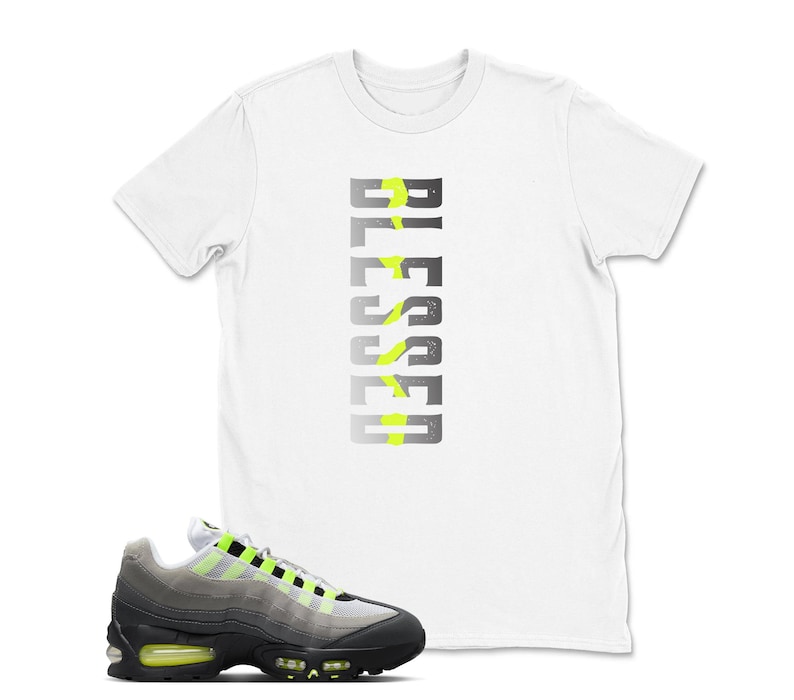 Op de afbeelding: Wit T-shirt met het woord "BLESSED" in een verticaal ontwerp, met neon groene accenten. Een paar grijze, zwarte en neon groene sportschoenen staan op de voorgrond, met een zwarte zool en neon groene accenten.