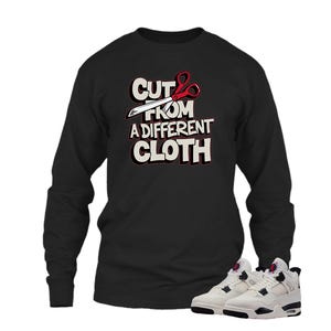 May include: Black long-sleeve shirt with the text "CUT FROM A DIFFERENT CLOTH" in white and red. The image also shows a pair of white and black sneakers.