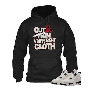 May include: Black hoodie with the text "CUT FROM A DIFFERENT CLOTH" in white and red. The hoodie has a front pocket and a drawstring hood. A pair of white and black sneakers are at the bottom of the image.