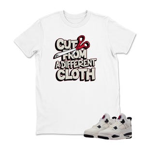 May include: White t-shirt with the text "CUT FROM A DIFFERENT CLOTH" in a bold, outlined font, featuring scissors. Below the shirt are white and black sneakers with red accents. The overall theme is streetwear fashion.