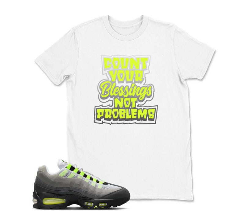 May include: White t-shirt with the text "Count Your Blessings Not Problems" in neon green and gray. A pair of gray, black, and neon green sneakers is in the foreground.