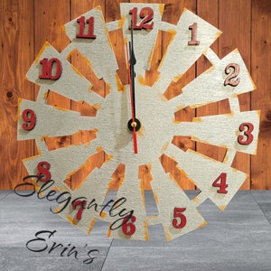 May include: A silver and gold windmill clock with red numbers. The clock is on a wooden background and has the words "Elegantly Erin's" written on the bottom.