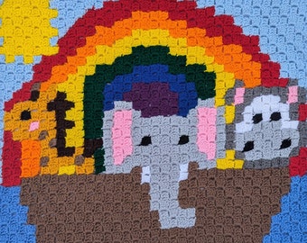 May include: A crocheted rainbow with a sun, an elephant, a lion, and a bear. The animals are all sitting on a brown boat.