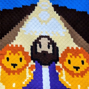 May include: A crocheted tapestry featuring a central figure with a brown beard and purple robe, flanked by two orange lions. The background includes a mountain range in shades of brown, tan, and blue.