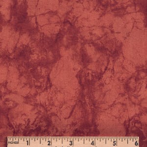 May include: A piece of fabric with a mottled, marbled pattern in shades of deep red and terracotta. A wooden ruler is positioned at the bottom edge, showing a scale of 6 inches, with the text Cindy Chock's Sewing Room printed on it.