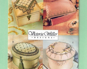 May include: A Vogue Craft pattern featuring four decorative box designs. The boxes vary in shape and color, including a square box with a green and beige design, and a round box with floral embellishments. The pattern number is 712.