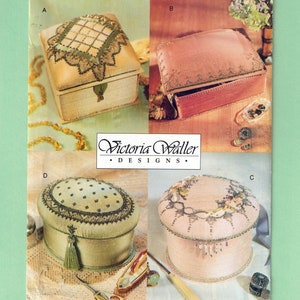 May include: A Vogue Craft pattern featuring four decorative box designs. The boxes vary in shape and color, including a square box with a green and beige design, and a round box with floral embellishments. The pattern number is 712.