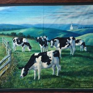 Op de afbeelding: Een schilderij van een landelijk tafereel met vijf zwart-witte koeien die grazen in een groen veld. Een houten hek loopt langs de linkerkant van het beeld. Op de achtergrond staat een witte kerk op een heuveltop. Het schilderij is gesigneerd met "Randy '93 McGovern".