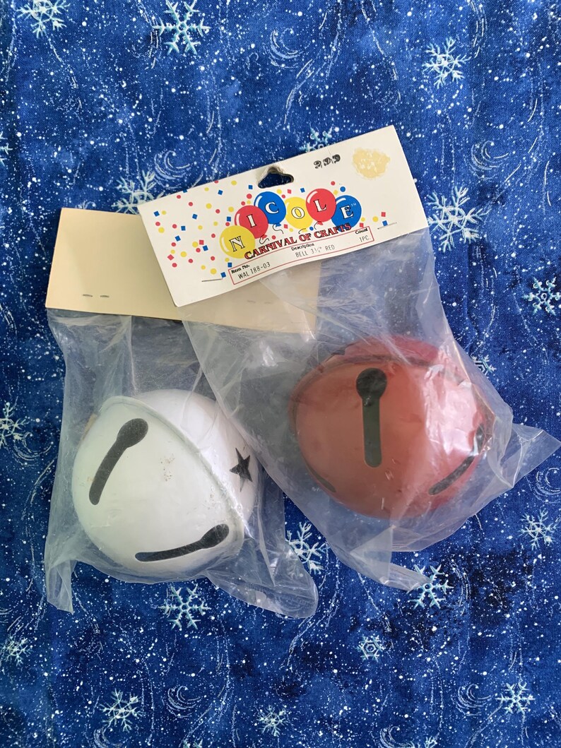 Puede incluir: Dos cascabeles redondos, uno blanco y otro rojo, cada uno con una ranura negra en forma de cruz. Est&aacute;n empaquetados en bolsas de pl&aacute;stico transparente con una tarjeta de cabecera Nicole Carnival of Crafts con gr&aacute;ficos de confeti.
