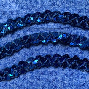 Könnte beinhalten: Nahaufnahme von drei Reihen marineblauer Paillettenborte mit gewelltem Rand. Die Pailletten sind in einem dunkleren Blauton gehalten und auf einem passenden Stoff aufgenäht. Der Hintergrund ist ein strukturierter blauer Stoff.