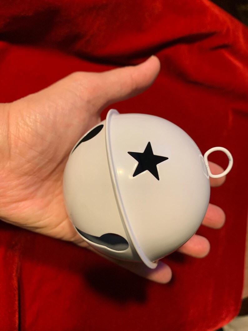 Puede incluir: Un cascabel de metal blanco con un recorte en forma de estrella en la mitad superior y una ranura curva tradicional en la parte inferior. El adorno esf&eacute;rico incluye un peque&ntilde;o lazo blanco en el lateral para colgar el objeto.