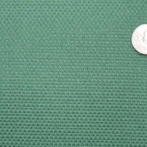 May include: A close-up of a green fabric with a textured surface. A US quarter is placed on the fabric for scale.