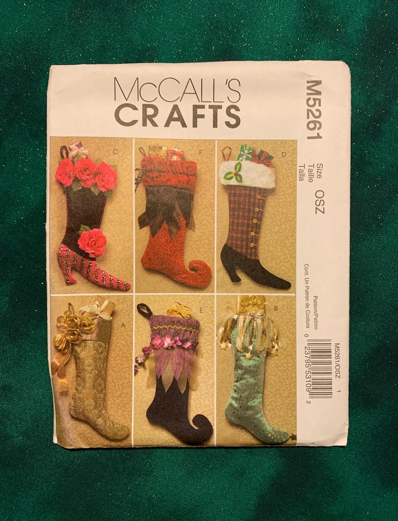 May include: McCall's Crafts M5261 sewing pattern envelope featuring six variations of decorative Christmas stockings. The designs include floral, plaid, and textured fabrics with various embellishments like ribbons, bows, and cuffs. The envelope displays the pattern number M5261 and size OSZ.
