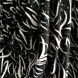 May include: Black fabric with a white abstract pattern and iridescent sequins.