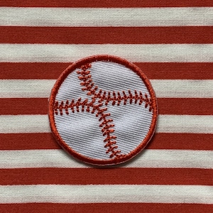 Può includere: Toppa da baseball bianca con cuciture rosse su uno sfondo di tessuto a righe rosse e bianche.