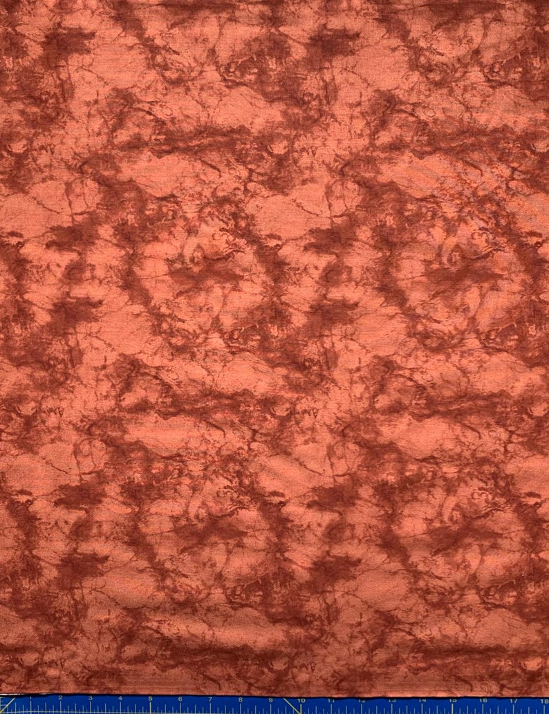 May include: A piece of fabric featuring a mottled, marbled pattern in shades of burnt orange and deep reddish-brown. The surface has a textured appearance with irregular, swirling dark lines distributed across the lighter orange base.