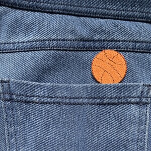 Può includere: Primo piano di una tasca di jeans blu con una toppa arancione da basket cucita su di essa.