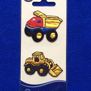 May include: Two iron-on patches featuring yellow construction vehicles. The first patch is a yellow dump truck with a red cab and blue wheels. The second patch is a yellow bulldozer with black wheels. The patches are on a white card with the text "Wrights Applique Application".