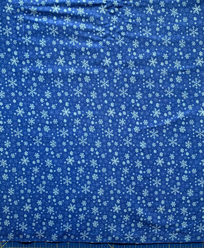 May include: A blue fabric featuring a repeating pattern of white snowflakes in various sizes and intricate designs. The textile displays a dense, scattered arrangement of these winter-themed shapes across the entire surface area.