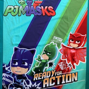 May include: A turquoise blue fabric with a colorful graphic print of the cartoon characters from the show "PJ Masks". The characters are wearing masks and costumes. The text "PJ Masks" is printed in large letters at the top of the fabric. The text "Ready for Action" is printed in large letters at the bottom of the fabric. The characters are shown in action poses with the text "Whoosh", "Swosh", and "Swoosh" printed next to them.