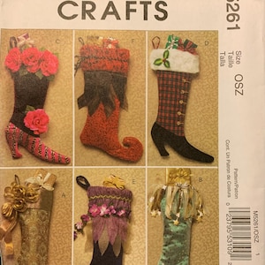May include: McCall's Crafts M5261 sewing pattern envelope featuring six distinct Christmas stocking designs. The illustrations show various styles including floral, plaid, and metallic fabrics with decorative accents like ribbons, faux fur, and curled toes.