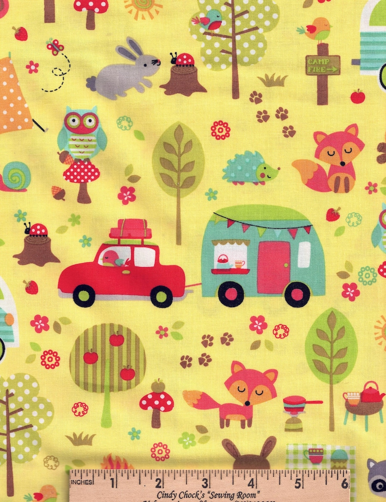 May include: Yellow fabric with a whimsical woodland scene. Features a red car pulling a teal camper, along with foxes, owls, rabbits, and trees. The design includes mushrooms, flowers, and the text "CAMP FIRE". Measurements are in inches.
