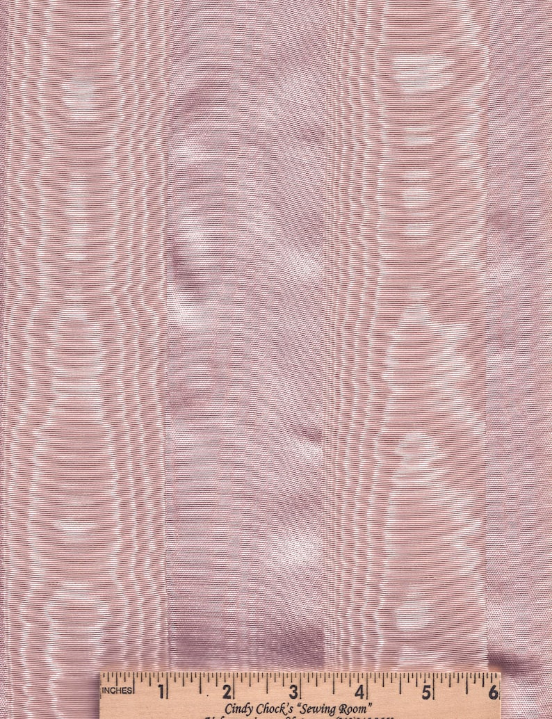 May include: Close-up of a pink fabric with vertical stripes and a subtle sheen. The fabric has a textured appearance with varying widths of stripes. A wooden ruler with inch measurements is at the bottom. The text "Cindy Chock's Sewing Room" is visible.