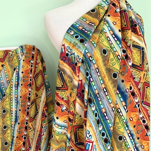 May include: A colourful fabric with a geometric pattern in shades of orange, yellow, blue, green, and red. The pattern features a repeating design of squares, triangles, and circles.