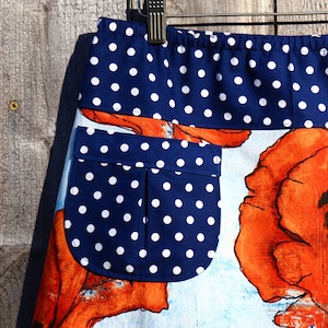 Könnte beinhalten: Ein blauer und weißer Tupfenrock mit weißem Hintergrund und einem Mohnblumenmuster. Der Rock hat eine Tasche auf der linken Seite.