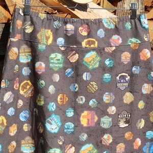 May include: A dark gray skirt with a pattern of colorful national park patches. The patches feature names like "Yellowstone", "Olympic", "Great Smoky", and "Yosemite".