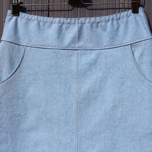 May include: A light blue denim skirt with two front pockets and a waistband.
