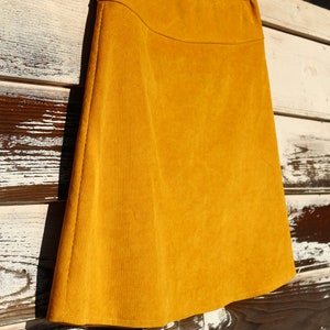 May include: A mustard yellow corduroy skirt hanging on a hanger. The skirt is a-line and has a simple design.