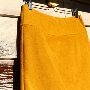 May include: A mustard yellow corduroy skirt hanging on a hanger. The skirt is a-line and has a simple design.