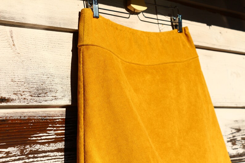 May include: A mustard yellow corduroy skirt hanging on a hanger. The skirt is a-line and has a simple design.