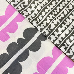 Puede incluir: Dos muestras de tela con diseños distintos. Una presenta un diseño repetitivo de formas blancas sobre un fondo gris oscuro. La otra tiene un patrón de grandes formas estilizadas en forma de pétalo, en rosa y gris sobre fondo blanco.