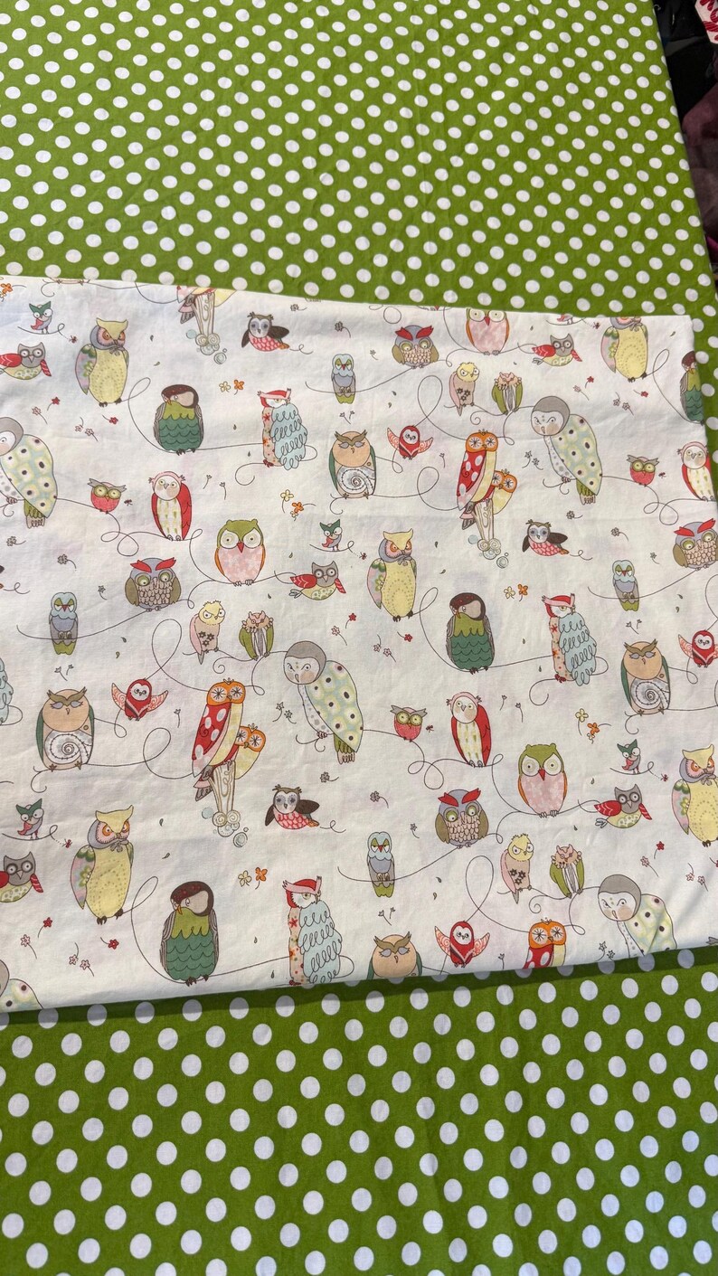 May include: White fabric with a repeating pattern of colorful owls in various poses, connected by whimsical lines. The owls feature a range of colors including green, red, yellow, and brown. The fabric is set against a green polka dot background.