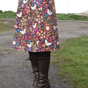 May include: A brown skirt with a colorful floral and bird print. The skirt is knee-length and has a fitted waist. The person is wearing brown boots with laces.
