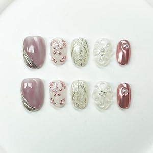 Può includere: Set di dieci unghie finte con diversi design. Le unghie sono rosa, bianche e argentate con glitter e motivi floreali.