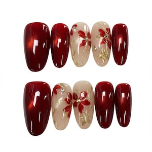 Peut inclure: Un ensemble d'ongles ovales à presser. Les ongles alternent entre un rouge profond et une base nude avec des motifs floraux rouges et des accents dorés. Certains ongles ont un effet scintillant.